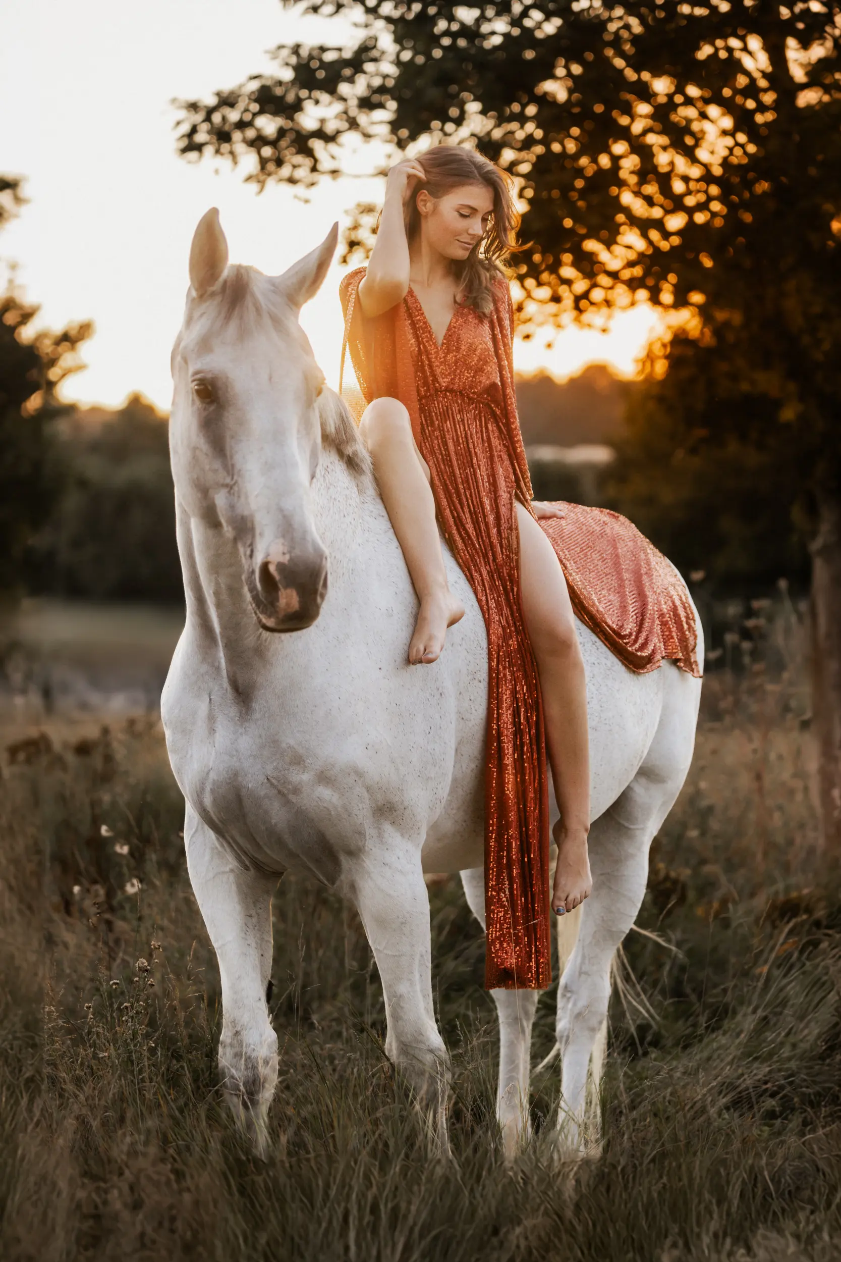 Frau im glitzernden Kleid im Sonnenlicht auf Pferd