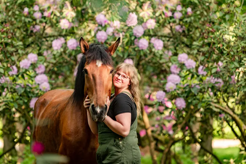 Frau umarmt Pferd vor Blumen